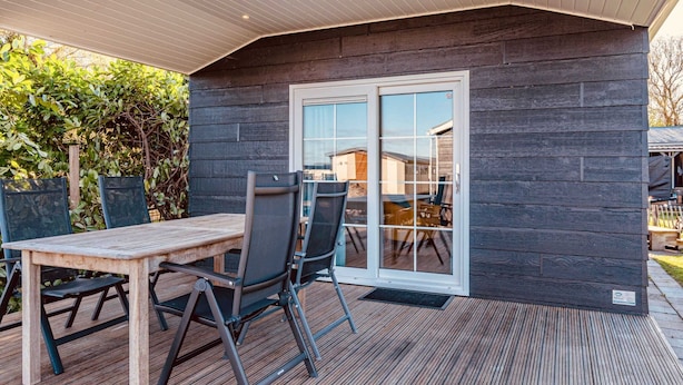 A covered outdoor patio with a wooden table and chairs, a sliding glass door, and a dark wooden wall. - Holiday Home With Terrace in Giethoorn (Giethoorn)