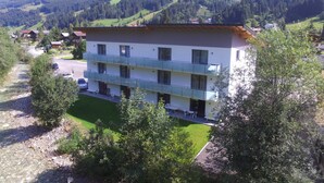 A multi-story hotel with a balcony on the second floor, surrounded by greenery and mountains in the background.