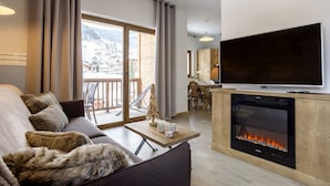 A living room with a sofa, a fireplace, a TV, and a view of a snowy mountain. - Apartment in Beaufort With Spa & Mountain Views (Beaufort)