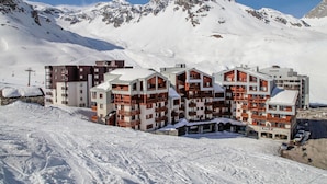 Une station de montagne enneigée, avec des bâtiments à plusieurs étages, des remontées mécaniques et un ciel dégagé.