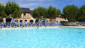 Une piscine entourée d’arbres et d’un bâtiment, avec des chaises longues et des parasols.