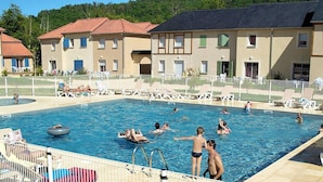 Une piscine avec des chaises longues et, au fond, un bâtiment doté d’un toit recouvert de tuiles.