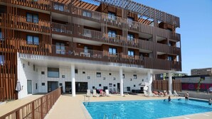 En modern byggnad med en swimmingpool, balkonger och ett takförsett område med solstolar.