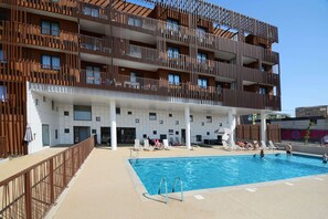A modern building with a swimming pool, balconies, and a covered area with lounge chairs. - Modern Seaside Apartment (Sète)