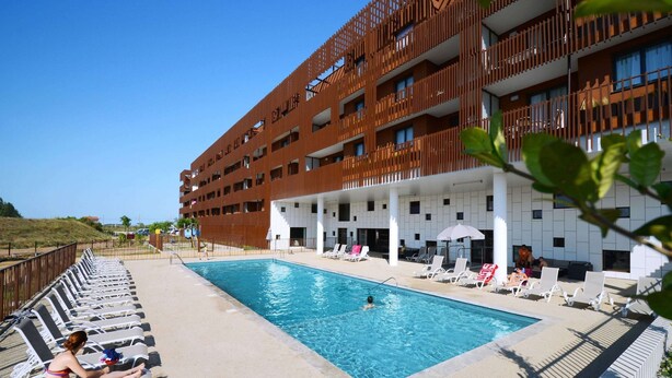 Ett hotell med en swimmingpool, solstolar och en modern byggnadsfasad.