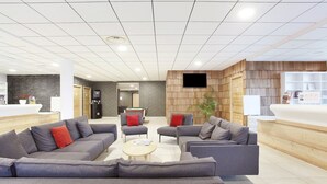 A modern lobby with sofas, a coffee table, a reception desk, and a TV mounted on a wooden wall. - Chic Chalet-style Apartment (La Clusaz)