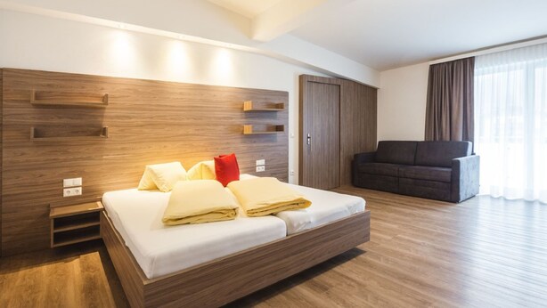 A modern hotel room with a large bed, wooden headboard, and a dark-colored sofa. - Apartment in Kleinarl Near Ski Slopes (Kleinarl)