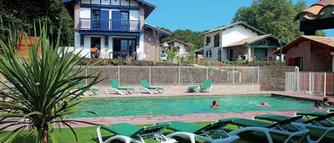 Uma área de piscina com espreguiçadeiras, uma palmeira e um prédio com varanda azul.