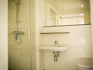 Ett badrum med en dusch som är avskärmad med glasväggar, ett vitt handfat och en toalett.