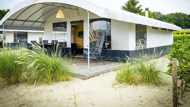 A modern beach house with a covered patio, outdoor seating, and a wooden deck. - Tent Lodge Near Loonse & Drunense Dunes (Udenhout)