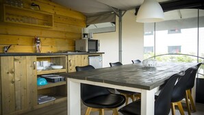 A modern kitchen with wooden cabinetry, a dining table with black chairs, and a large window offering a view of the outdoors. - Tent Lodge Near Loonse & Drunense Dunes (Udenhout)
