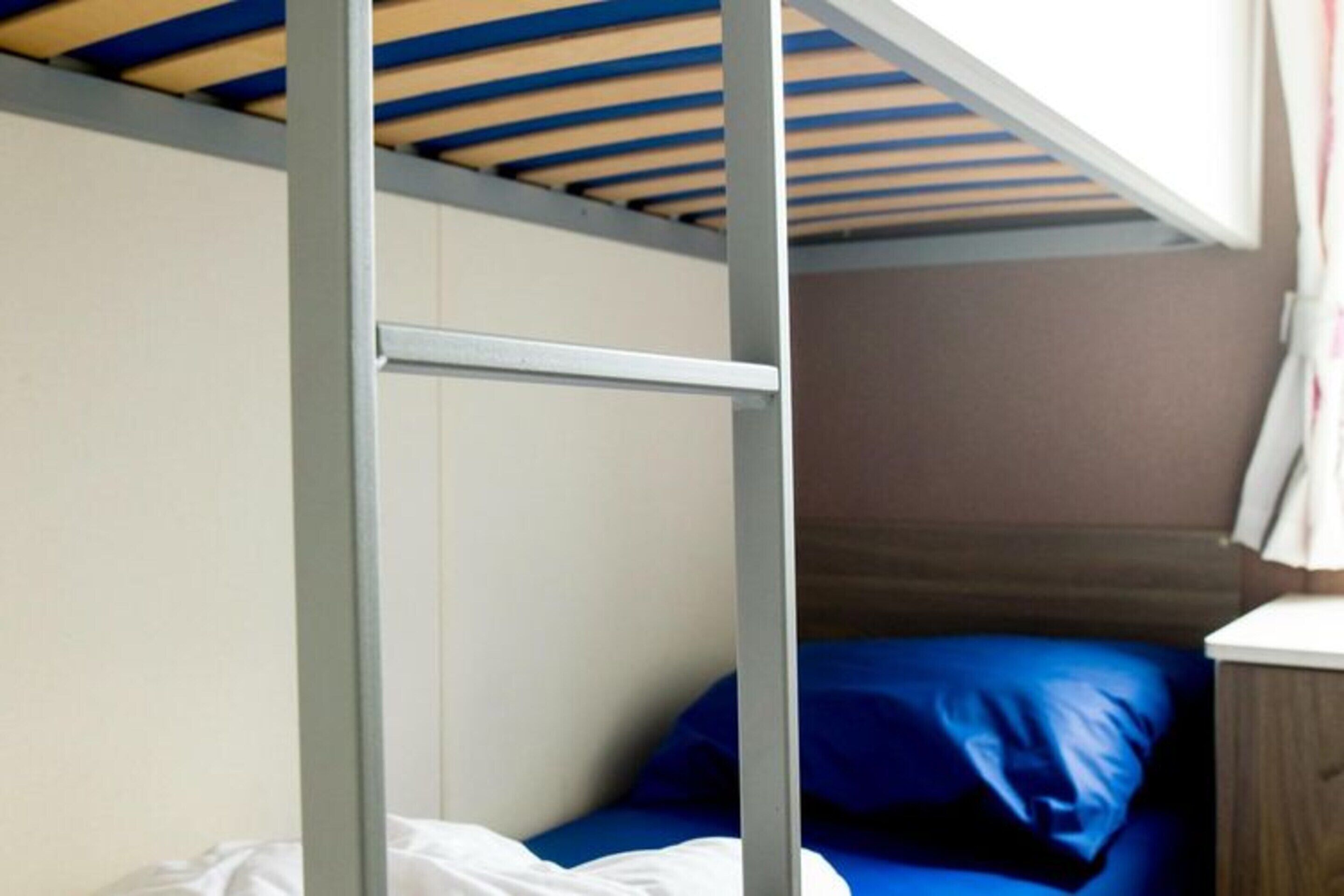 Un lit superposé avec un plafond en bois et un lit simple avec un matelas bleu.