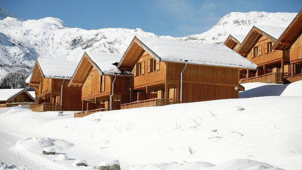 Ein holzgetäfeltes Chalet-Hotel mit mehreren Balkonen vor einer verschneiten Bergkulisse.