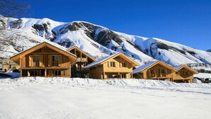 Eine Reihe Holzhütten mit Balkonen vor der Kulisse schneebedeckter Berge.