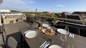 A rooftop terrace with a table set for dining, overlooking a cityscape and the sea. - Apartment in Domburg Near Sandy Beaches (Domburg)