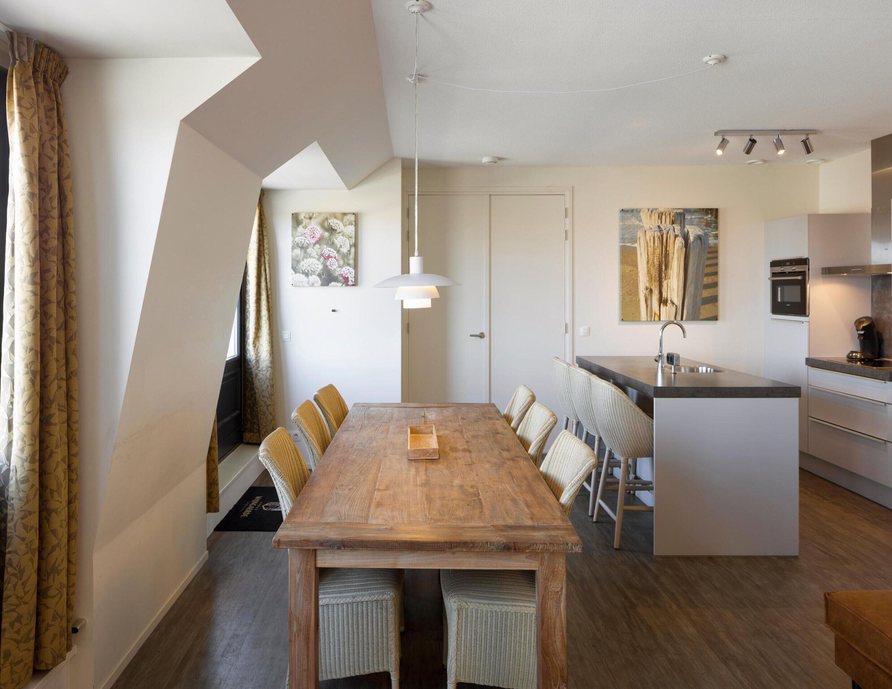 A modern kitchen with a central island, a dining area with a wooden table and wicker chairs, and a large window with curtains.