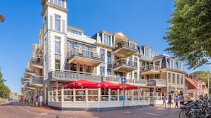 A multi-story building with a prominent tower, balconies, and outdoor seating areas with red umbrellas. - Apartment in Domburg Near Sandy Beaches (Domburg)