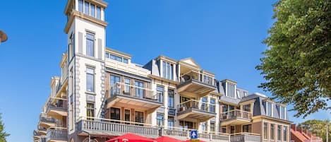 Un edifici d'àmbitós caràcter amb una torre destacada, balcons i zones d'esbarjo a l'aire lliure amb paraigües vermells.