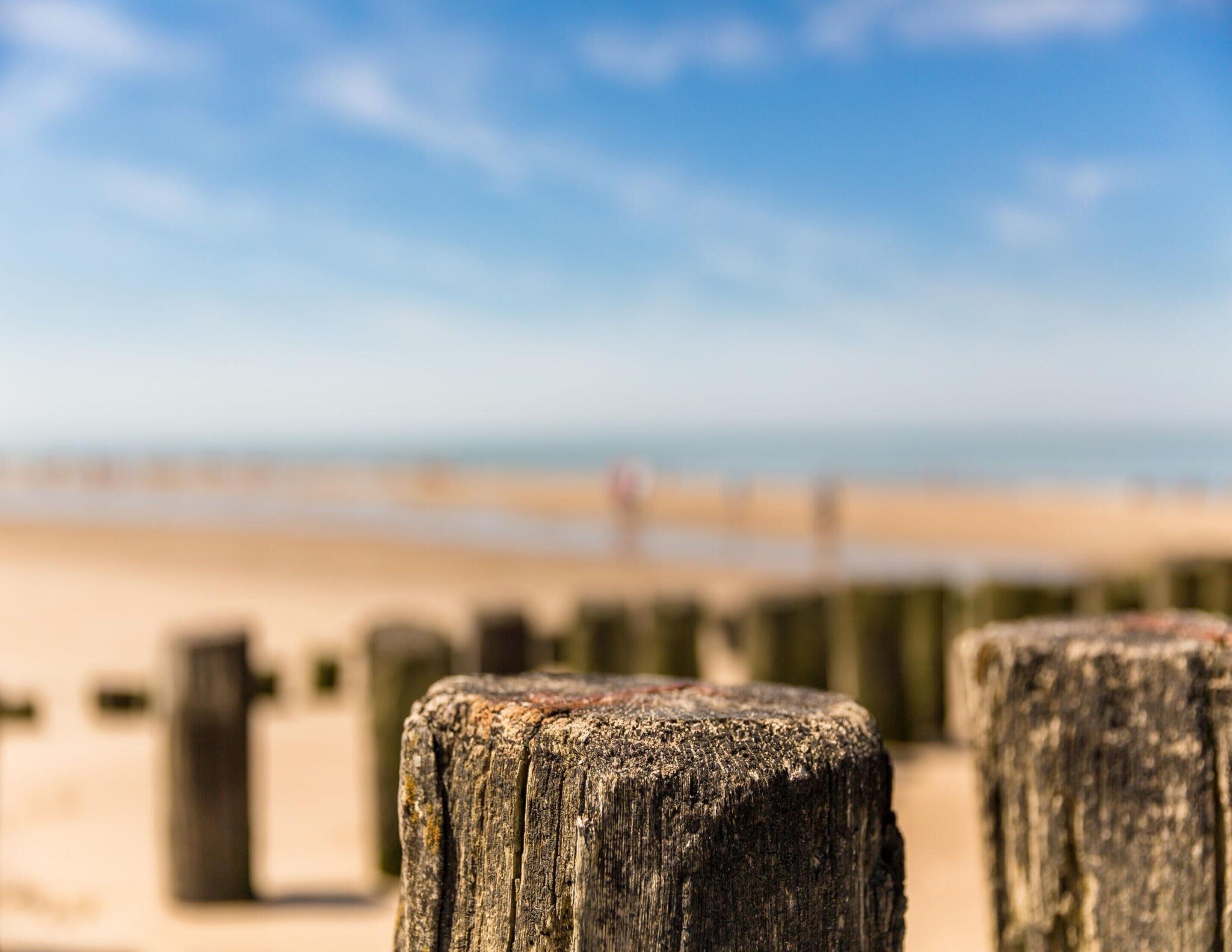 Ein Holzpfosten am Strand mit blauem Himmel und weiter Meer im Hintergrund.