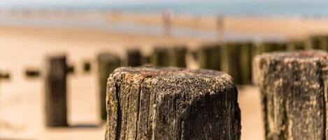 Ein Holzpfosten am Strand mit blauem Himmel und weiter Meer im Hintergrund.