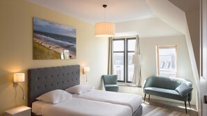 A modern hotel room with a large bed, two bedside tables, a desk, a chair, a floor lamp, and a large window with a view of the city. - Apartment in Domburg Near Sandy Beaches (Domburg)