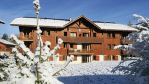 Ein mehrstöckiges Holzgebäude mit Balkonen, umgeben von schneebedeckten Bäumen.