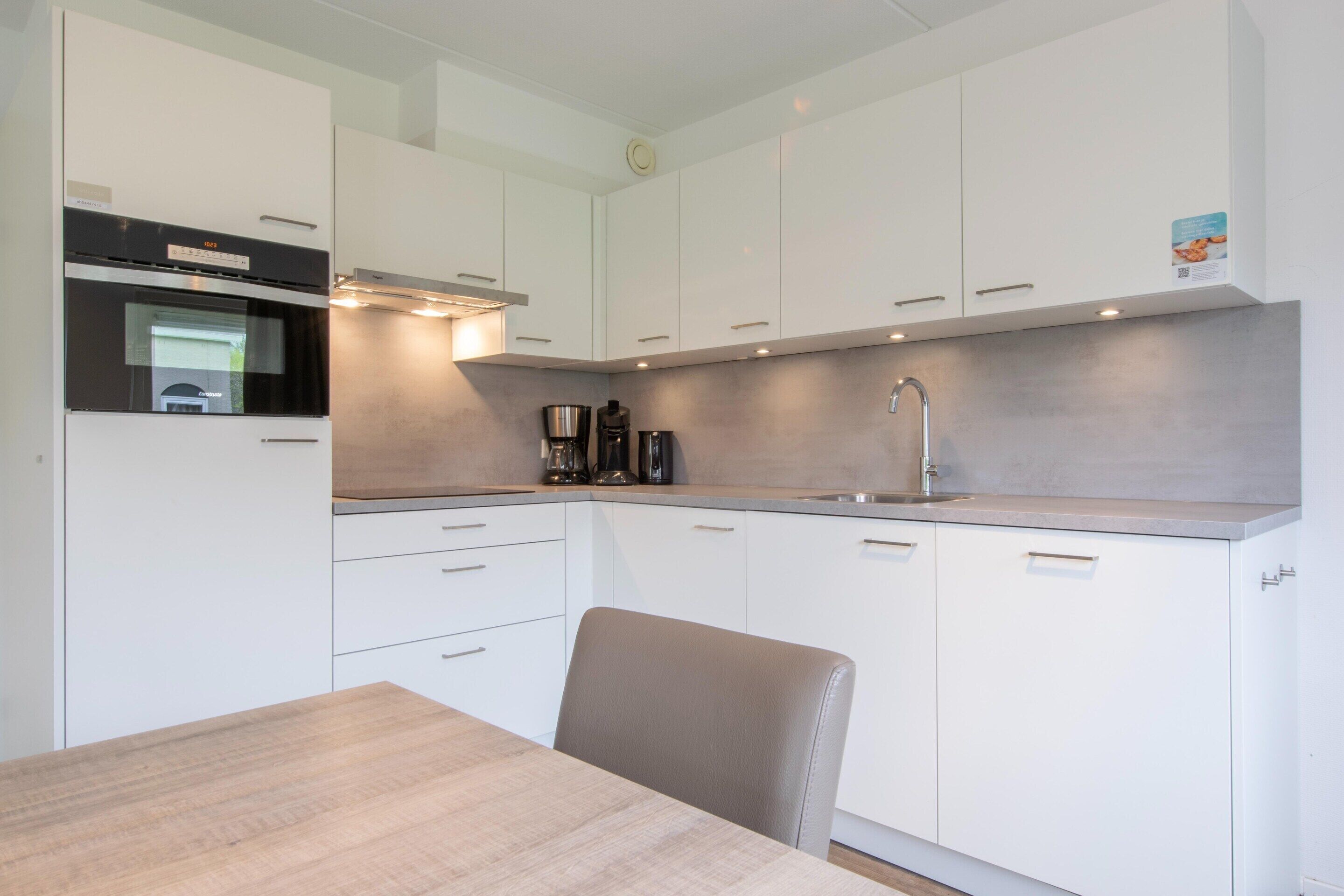 A modern kitchen with white cabinets, a built-in oven, a coffee maker, and a sink.