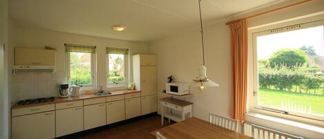 A kitchen with a wooden table, white cabinets, a microwave, and a window with curtains.