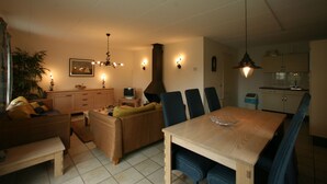 Una sala de estar con mesa de comedor, sillas, sofá, televisor y zona de cocina.