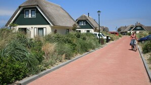 Un camino bordeado por casas tradicionales con tejados de paja, un ciclista y coches estacionados.