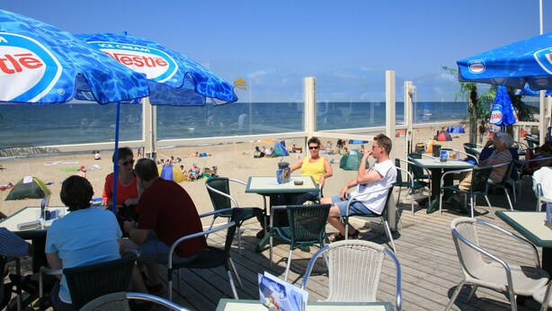 Un restaurante frente a la playa con terraza y sombrillas.