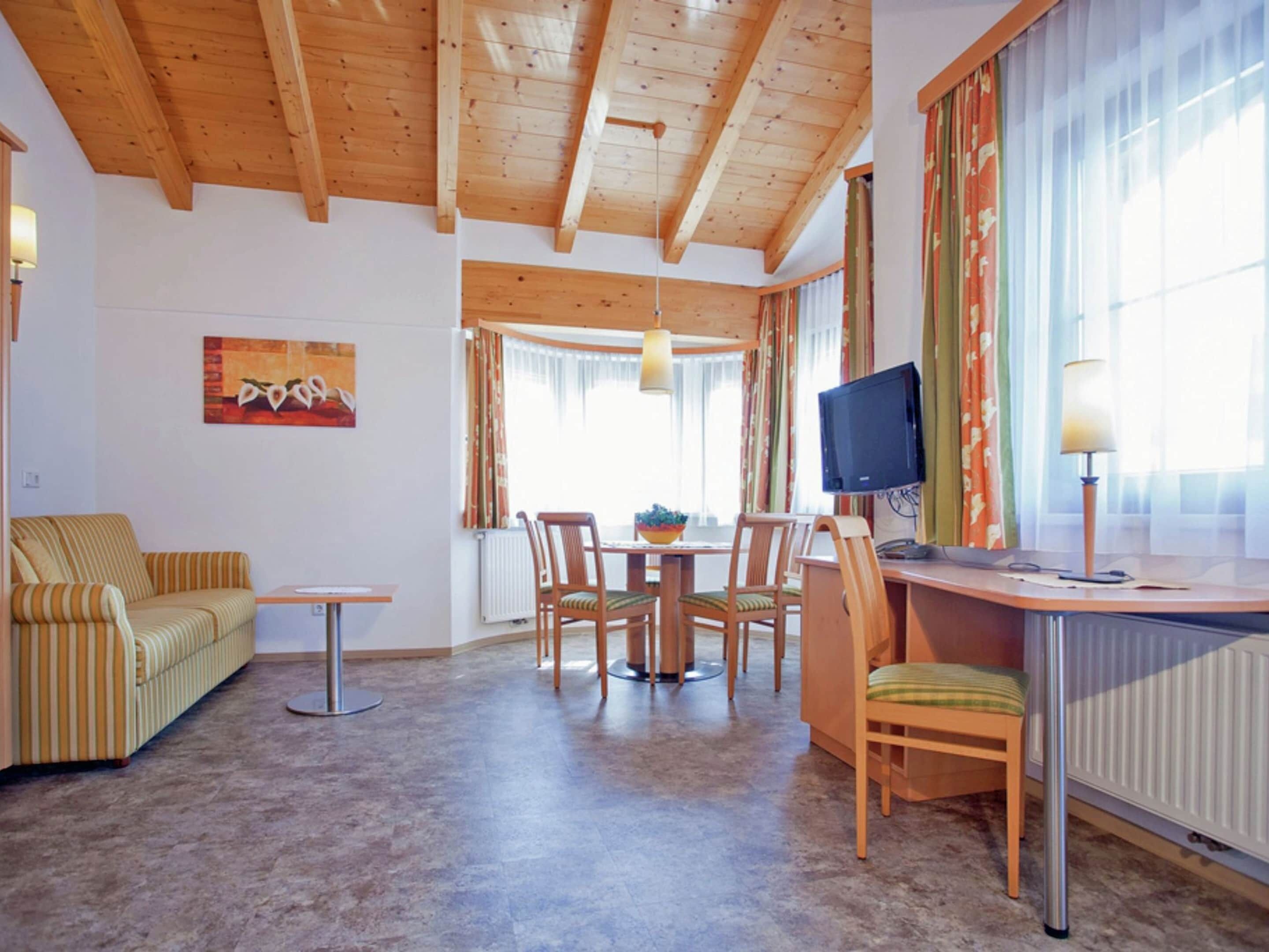 Un accogliente soggiorno con soffitto in legno, un'area pranzo con tavolo e sedie, un divano e un televisore su una scrivania.