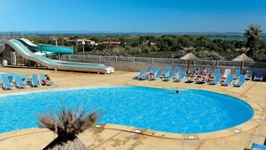 A swimming pool with lounge chairs, a water slide, and a view of the landscape. - Cap D'agde Bungalow Retreat (Agde)
