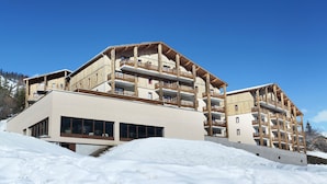 Ein mehrstöckiges Hotel mit Balkonen, großen Fenstern und einer Skipiste im Hintergrund.