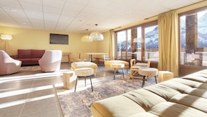 Ein modernes Wohnzimmer mit einer Couch, Sesseln, einem Tisch und Blick auf Berge durch große Fenster.