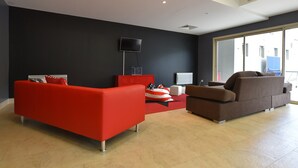 A modern living room with a red sofa, a brown sofa, and a red ottoman. There is a flat-screen TV mounted on the wall, a window with a view of the outside, and a ceiling vent. - Chalet in Isola Near Ski Slopes (Isola)