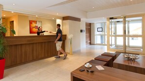 A hotel reception area with a wooden reception desk, a vase of flowers, and a seating area with a table and chairs. - Chalet in Isola Near Ski Slopes (Isola)