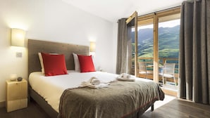 Una camera d'albergo con un letto, abat-jour, comodino e vista su un paesaggio montuoso attraverso una grande finestra.