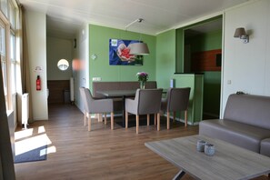 Un coin repas avec une table et des chaises, un canapé, une petite table avec deux tasses et une lampe fixée au mur.