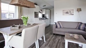 A modern living room with a sofa, a dining table with chairs, a kitchen area, and a large window. - Chalet in Netherlands With Private Sauna (Voorthuizen)