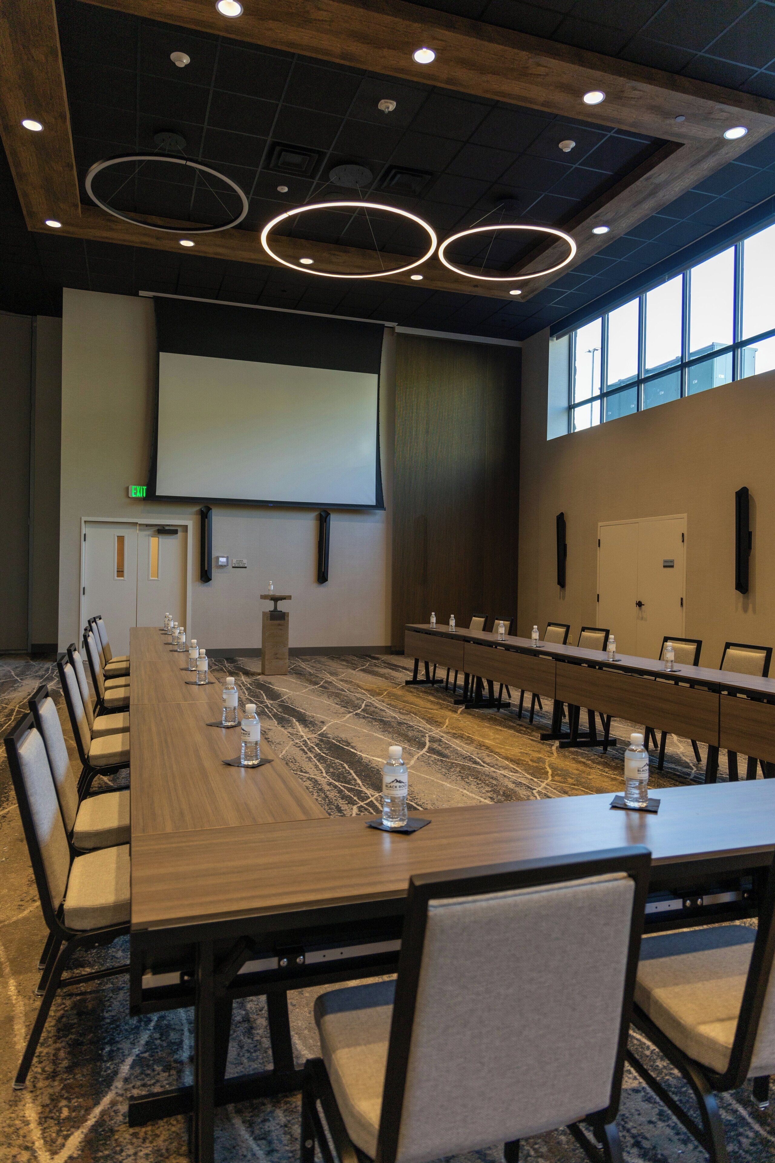 A conference room with a long table, chairs, a projector screen, and a large window.