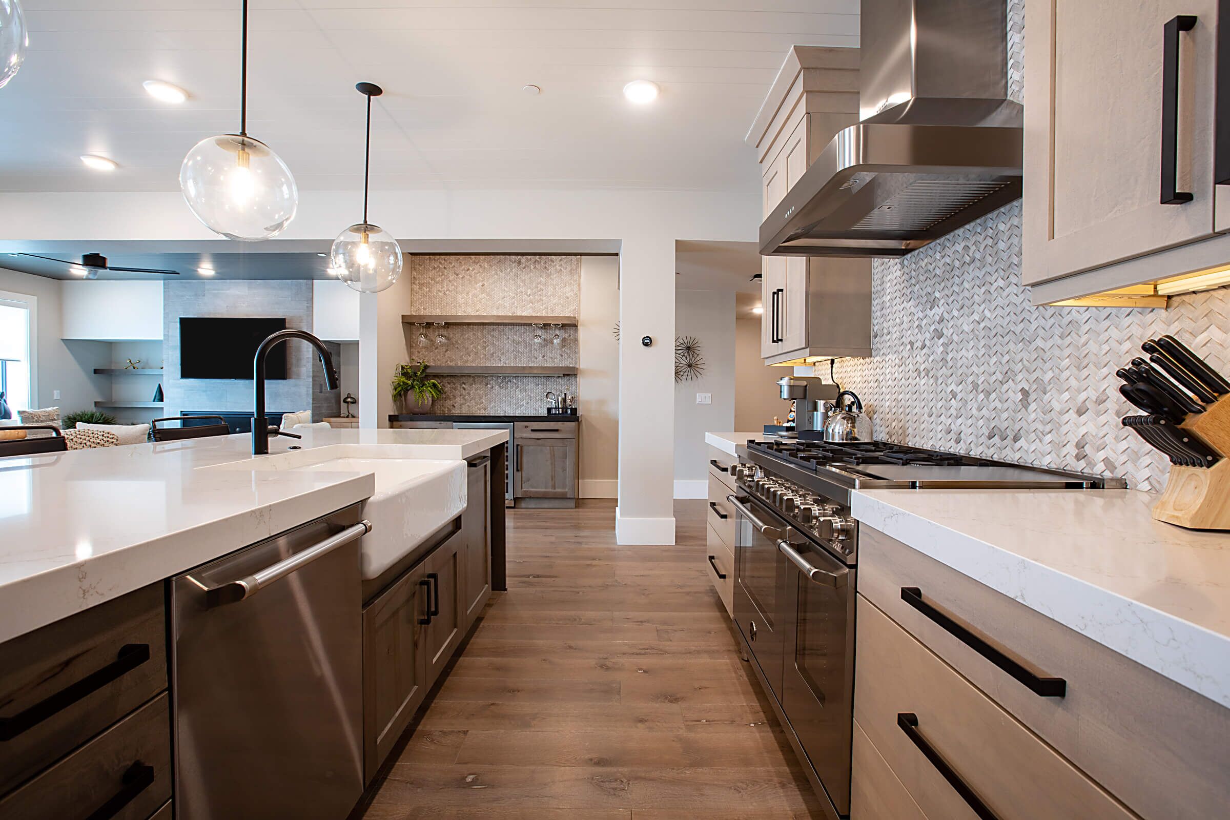 A modern kitchen with stainless steel appliances, a large island, pendant lighting, and a herringbone tile backsplash.