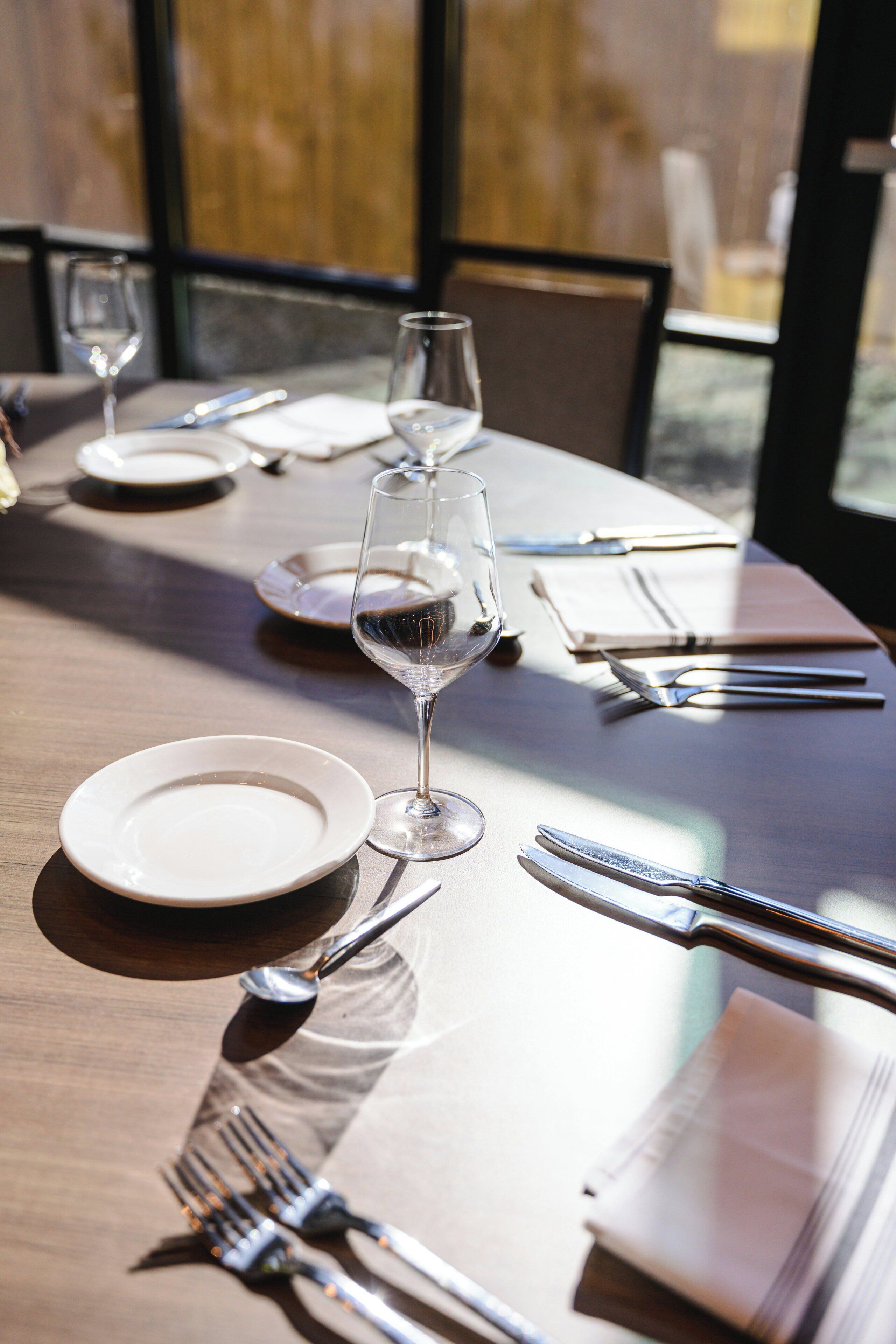 Mesa posta para refeição com pratos, talheres e taças de vinho.