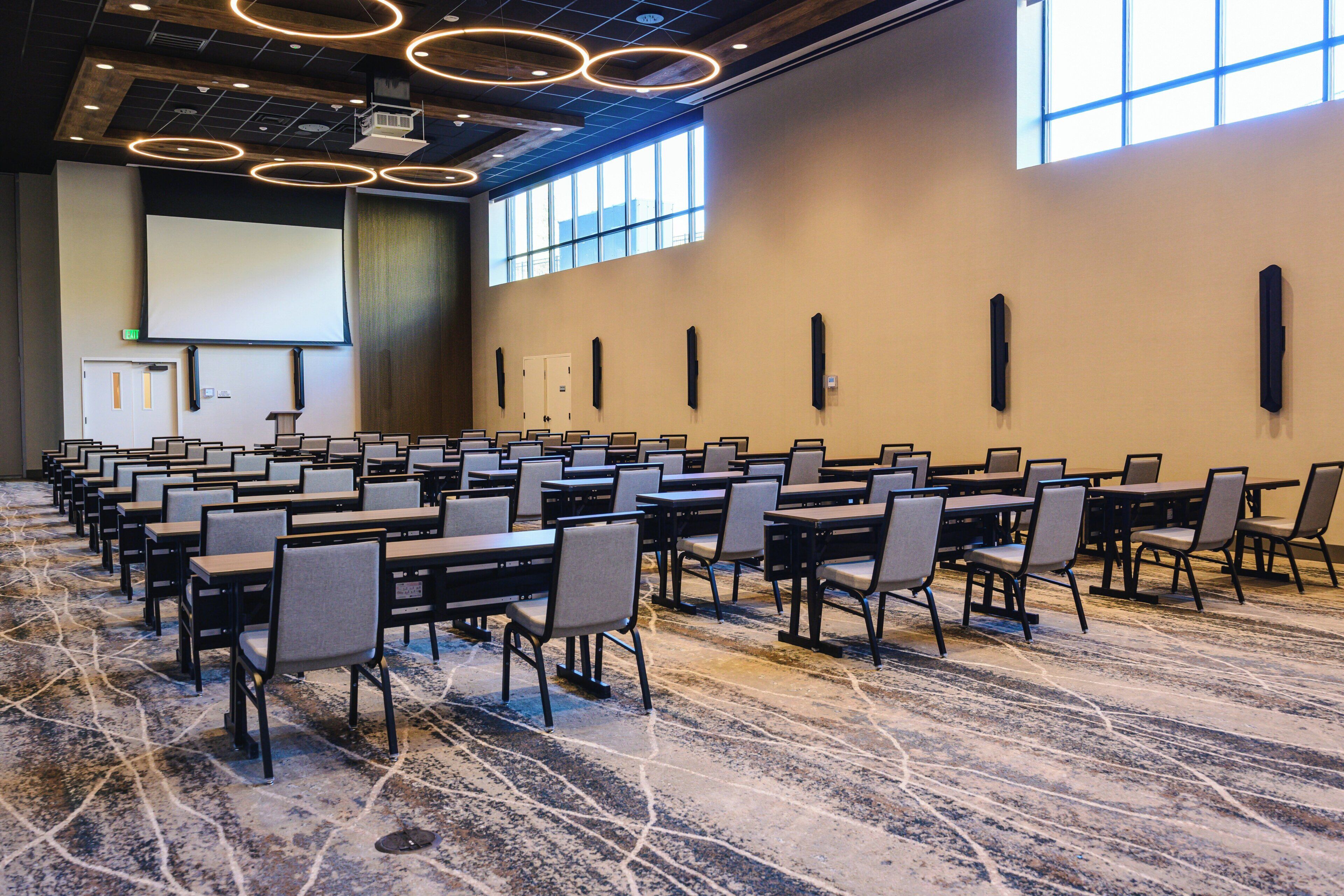 A conference room with rows of tables and chairs, a projector screen, and a large window.