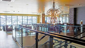 A spacious indoor area with a modern staircase, seating, and a large window offering a view of snow-covered hills.