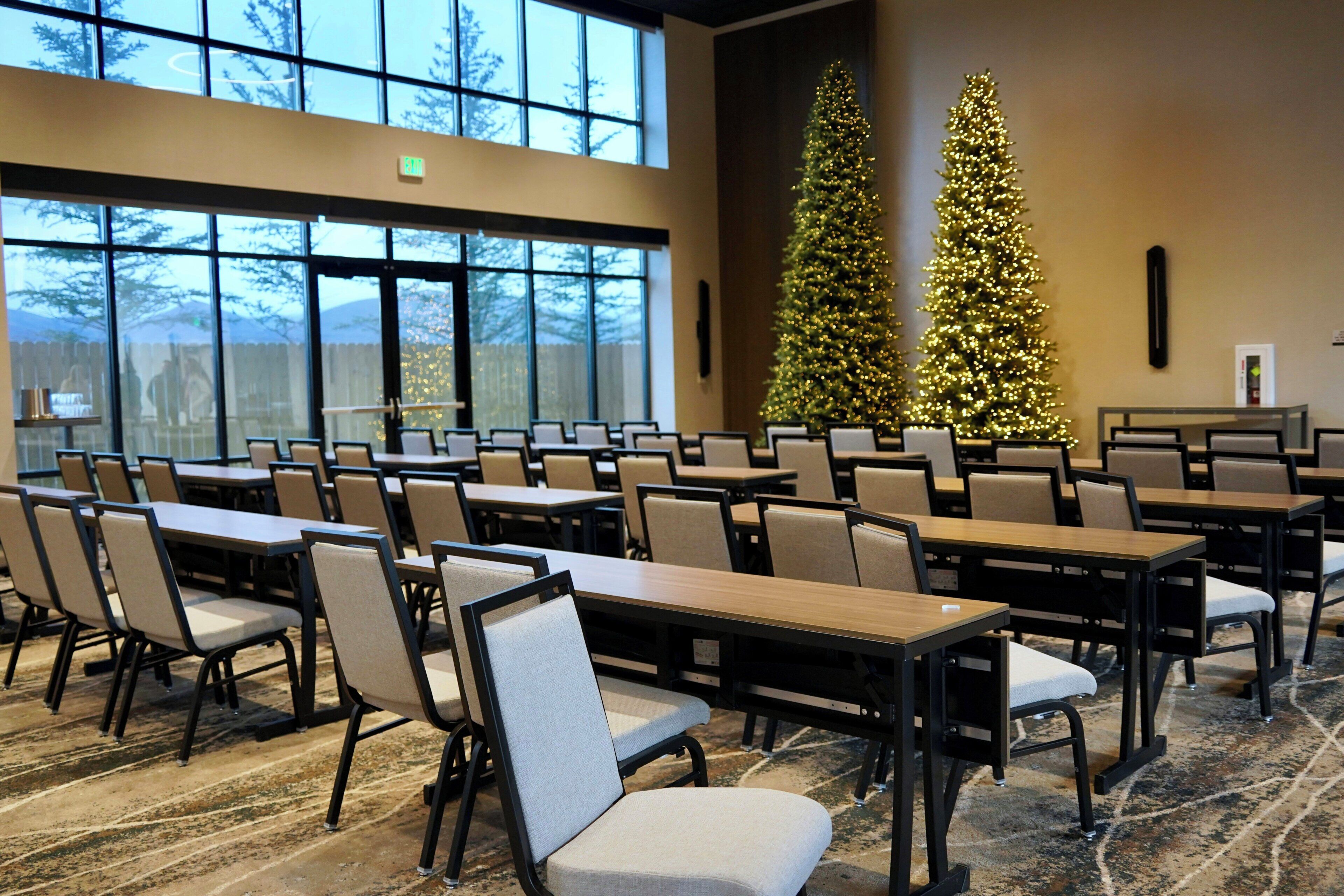 A conference room with tables and chairs, large windows, and two Christmas trees.