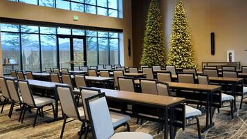 A conference room with tables and chairs, large windows, and two Christmas trees.