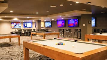 A pool table with balls, a bar area with stools, and multiple screens displaying content.