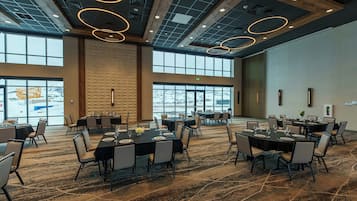 A spacious conference room with multiple tables set for dining, large windows offering a view of a snowy landscape, and a modern ceiling design with circular light fixtures.