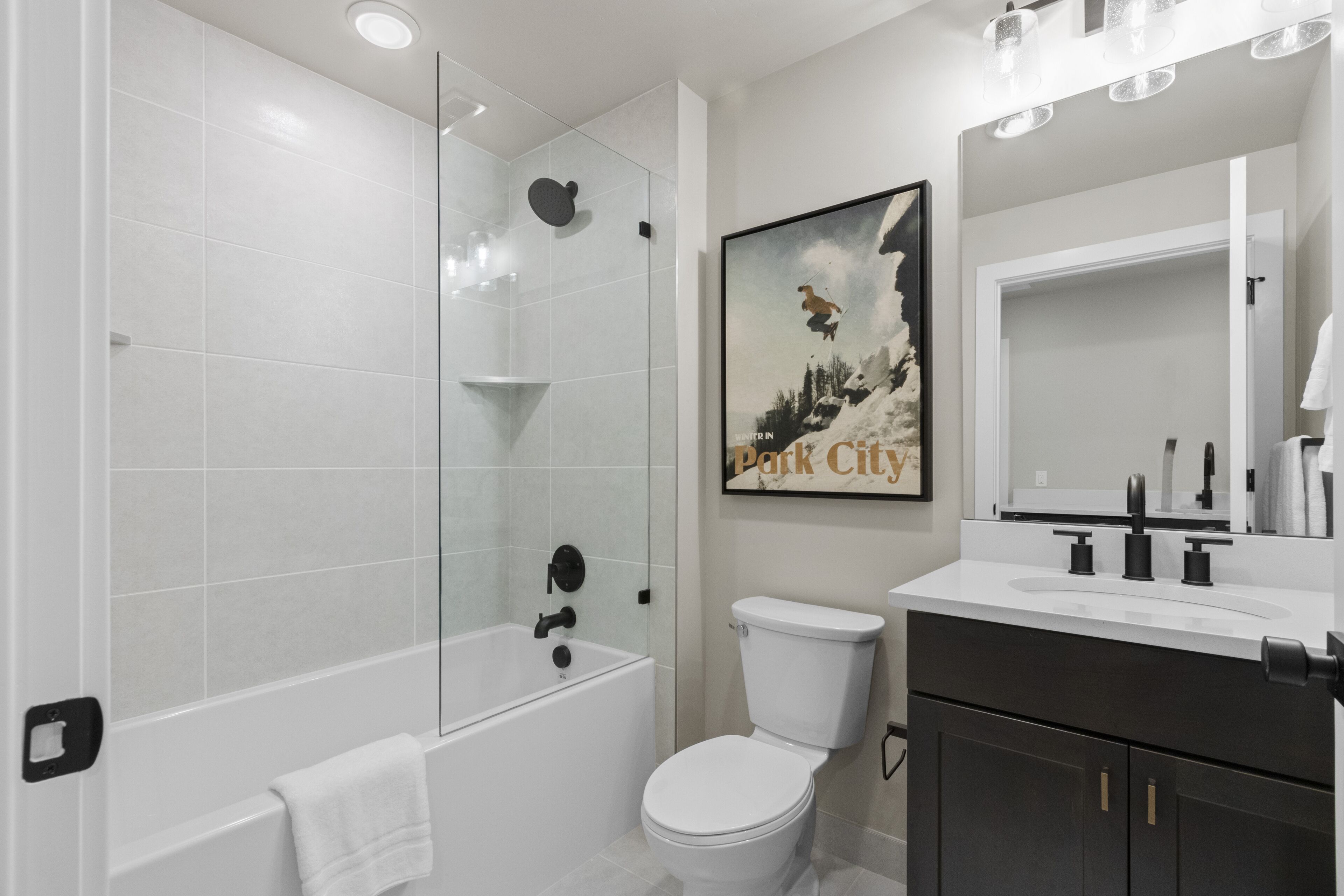 A modern bathroom with a glass-enclosed shower, a white toilet, and a dark vanity with a large mirror.